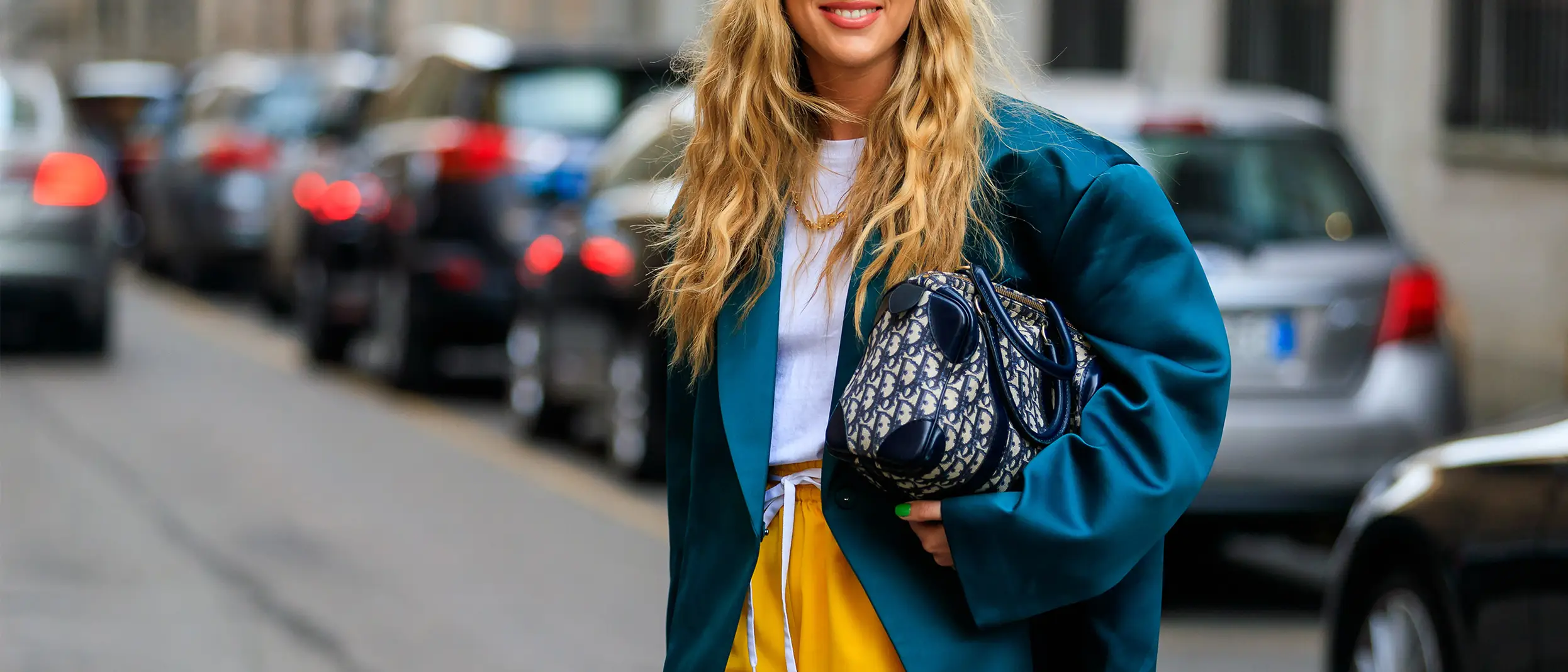 Woman wearing a teal blazer, yellow skirt, and holding a Dior handbag, smiling on a city street Woman wearing a teal blazer, yellow skirt, and holding a Dior handbag, smiling on a city street