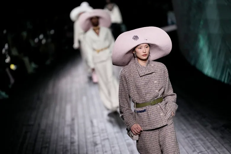 Model in a dramatic black cape with ruffled high collar and oversized bows walking down the runway. Model in a dramatic black cape with ruffled high collar and oversized bows walking down the runway.